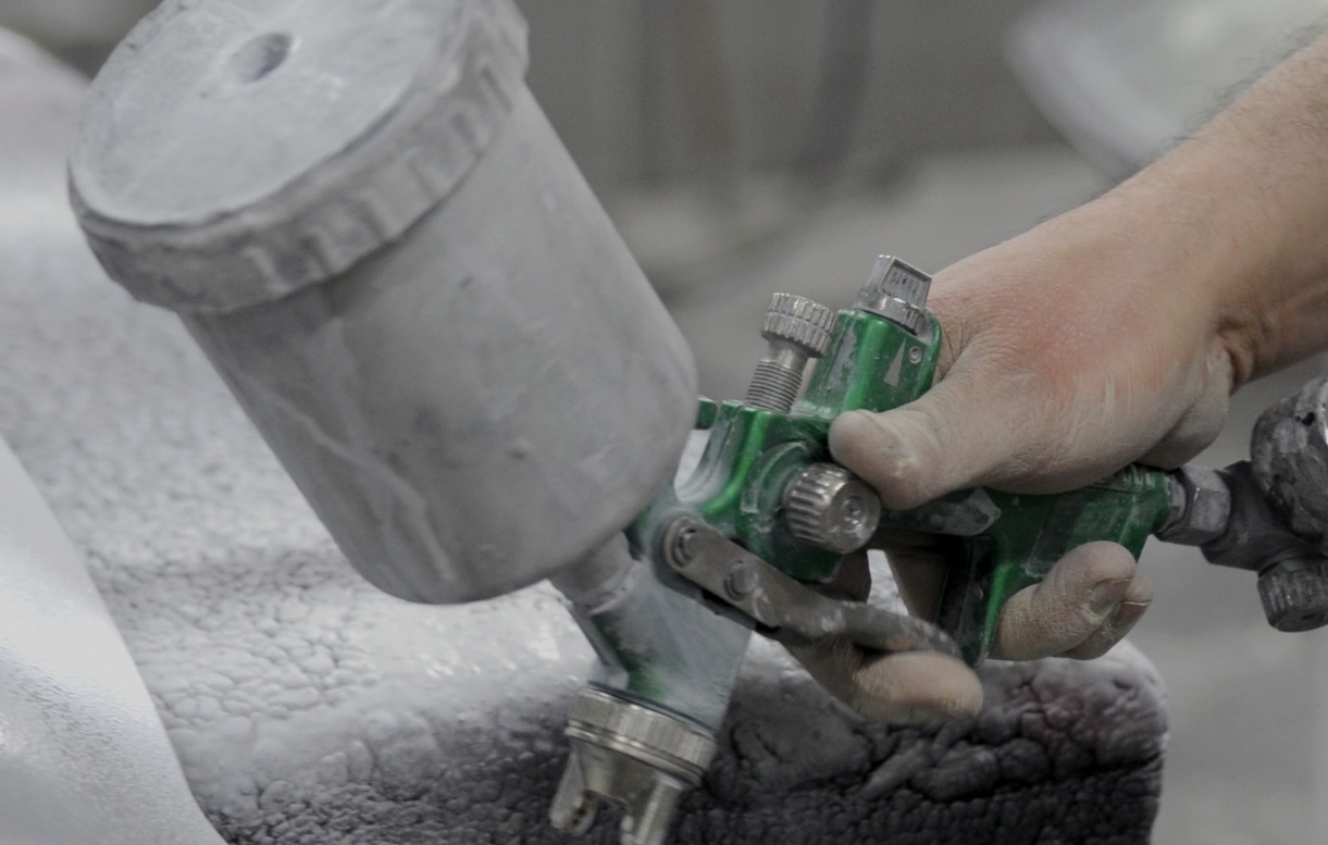 Aplica&ccedil;&atilde;o de revestimento autom&oacute;vel com pistola de pintura em ambiente industrial, ilustrando solu&ccedil;&otilde;es t&eacute;cnicas testadas diretamente na linha de produ&ccedil;&atilde;o.
